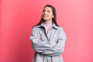 pretty young adult woman feeling happy, proud and hopeful, wondering or thinking, looking up to copy space with crossed arms