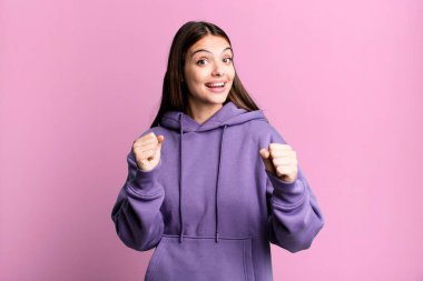 pretty young adult woman feeling shocked, excited and happy, laughing and celebrating success, saying wow!