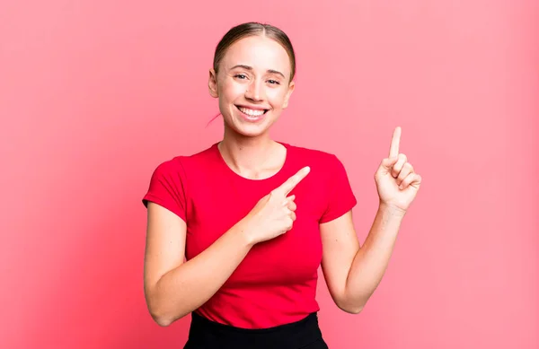 smiling happily and pointing to side and upwards with both hands showing object in copy space