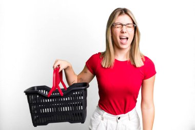 Genç ve güzel bir kadın agresif bir şekilde bağırıyor, çok kızgın görünüyor. boş alışveriş sepeti kavramı