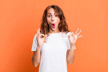 Genç, güzel bir kadın şok olmuş, şaşırmış ve şaşırmış hissediyor. İki eliyle de onay işareti yapıyor.