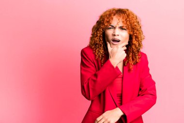 Kızıl saçlı güzel bir kadın. Ağzı ve gözleri açık ve elleri çenesinde. İş kadını kavramı