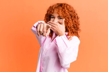 Kızıl saçlı güzel kadın sana gülüyor, kamerayı gösteriyor ve seninle dalga geçiyor ya da alay ediyor.