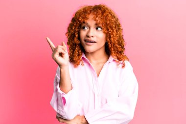 Kızıl saçlı güzel kadın mutlu bir şekilde gülümsüyor ve yan bakıyor, merak ediyor, düşünüyor ya da bir fikri var.