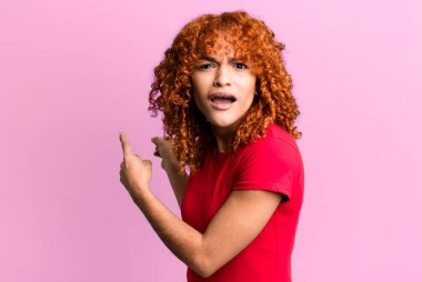 Kızıl saçlı, güzel bir kadın şaşkın ve şaşırmış hissediyor. Yandaki fotokopi alanını işaret ediyor. Şaşırmış, ağzı açık bir bakış.