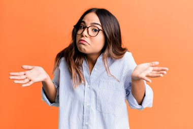 hispanic pretty woman feeling clueless and confused, having no idea, absolutely puzzled with a dumb or foolish look