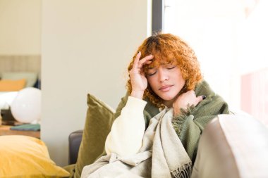 Genç kızıl saçlı, Latin, güzel bir kadın evdeki kanepede dinleniyor.