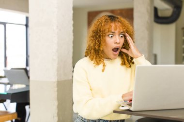 Genç kızıl saçlı, latin, güzel bir kadın evde dizüstü bilgisayarla geziyor.