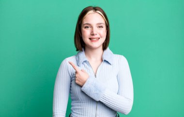 Genç, güzel bir kadın neşeyle gülümsüyor, mutlu hissediyor ve bir tarafı işaret ediyor.