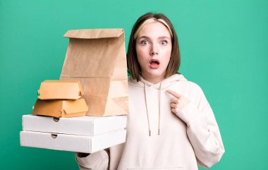 young pretty woman looking shocked and surprised with mouth wide open, pointing to self. take away fast food concept