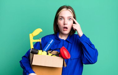young pretty woman looking surprised, realizing a new thought, idea or concept. housekeeper and toolbox concept