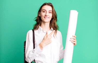 young pretty woman smiling cheerfully, feeling happy and pointing to the side. architect concept