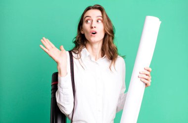 young pretty woman looking surprised and shocked, with jaw dropped holding an object. architect concept