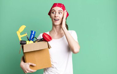 young pretty woman feeling happy, excited and surprised. housekeeper and toolbox concept