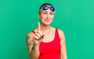 young pretty woman smiling and looking friendly, showing number one. swimmer concept