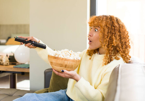 молодые рыжие волосы латинос красивая женщина ест попкорн на диване и смотреть фильм