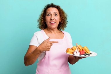 pretty middle age woman looking excited and surprised pointing to the side. home made waffles concept