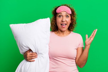 pretty middle age woman feeling happy and astonished at something unbelievable wearing pajamas night wear and a pillow