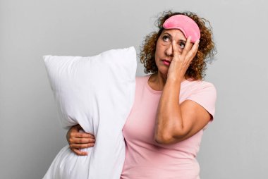 pretty middle age woman feeling bored, frustrated and sleepy after a tiresome wearing pajamas night wear and a pillow