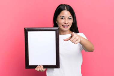 hispanic pretty woman pointing at camera choosing you with an empty blank frame
