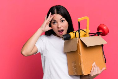 hispanic pretty woman looking happy, astonished and surprised with a tool box