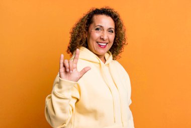 Orta yaşlı İspanyol bir kadın kendini mutlu, eğlenceli, kendinden emin, pozitif ve asi hissederek elle rock veya heavy metal işareti yapıyor.