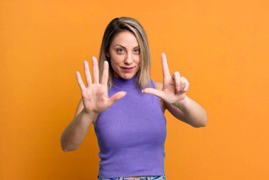 blonde adult woman smiling and looking friendly, showing number seven or seventh with hand forward, counting down