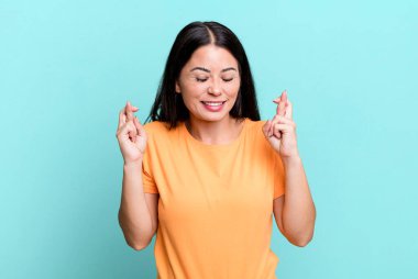 Güzel Latin bir kadın gülümsüyor ve endişeyle iki parmağını çaprazlıyor. Endişeli ve iyi şanslar diliyor.