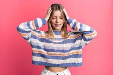 Sarışın, güzel bir kadın stresli ve hayal kırıklığına uğramış hissediyor, ellerinizi havaya kaldırıyor, yorgun, mutsuz ve migren ağrısı çekiyor.