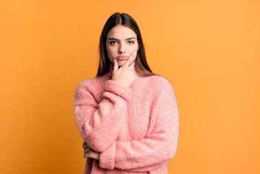 Güzel, genç bir kadın ciddi, düşünceli ve güvensiz görünüyor, bir kolu çapraz ve çenesi üzerinde, seçenekleri tartıyor.