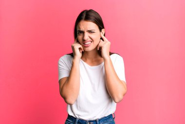 Güzel, genç bir kadın sinirli, stresli ve sinirli görünüyor, iki kulağını da sağır edici bir ses, ses ya da yüksek sesle kapatıyor.