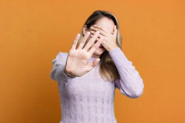 Yüzünü eliyle kapatıyor ve kamerayı durdurmak için diğer elini öne koyuyor, fotoğraf ya da resimleri reddediyor.