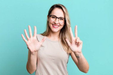 Gülümsüyor ve dost canlısı görünüyor, 8 ya da 8 numarayı gösteriyor, elleri önde, geriye doğru sayıyor.