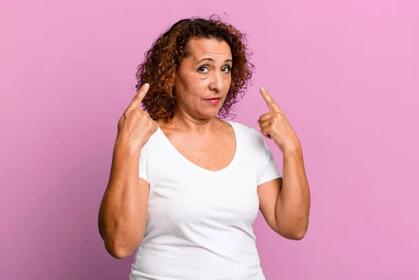 middle age hispanic woman with a bad attitude looking proud and aggressive, pointing upwards or making fun sign with hands