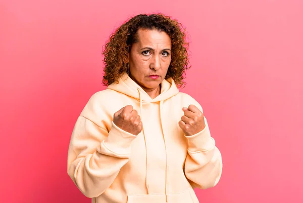 middle age hispanic woman looking confident, angry, strong and aggressive, with fists ready to fight in boxing position