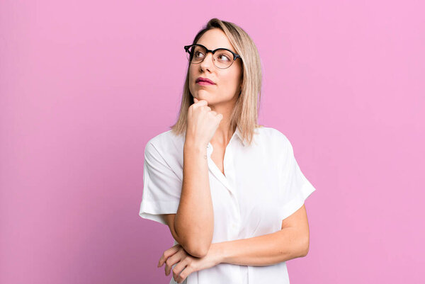 blonde adult woman feeling thoughtful, wondering or imagining ideas, daydreaming and looking up to copy space