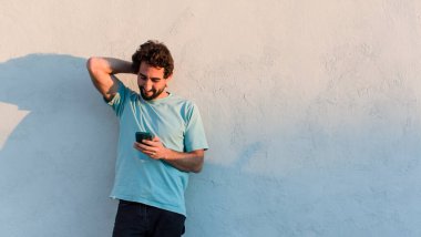 young bearded man using his smartphone against white wall background