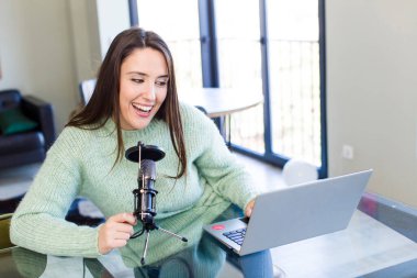 young pretty young adult influencer woman with a microphone and a laptop on a desk