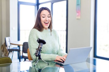young pretty young adult influencer woman with a microphone and a laptop on a desk