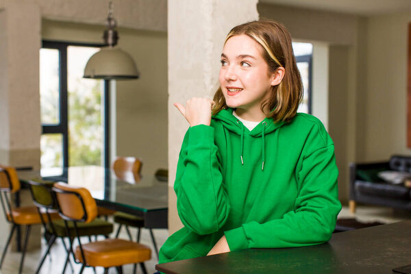 pretty caucasian woman smiling cheerfully and casually pointing to copy space on the side, feeling happy and satisfied. home interior concept