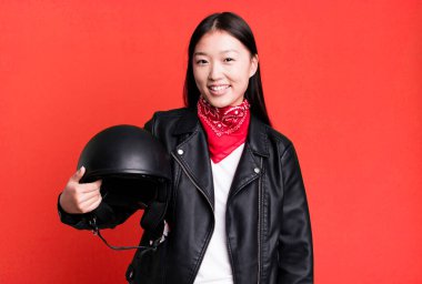 Genç, güzel, Asyalı bir kadın. Deri ceketli ve kask takan motosiklet sürücüsü.