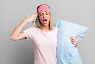 pretty blonde woman looking unhappy and stressed, suicide gesture making gun sign. pajamas and nightwear concept