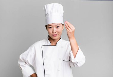 pretty asian woman making capice or money gesture, telling you to pay. restaurant chef concept