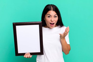 hispanic pretty woman looking desperate, frustrated and stressed with an empty blank frame