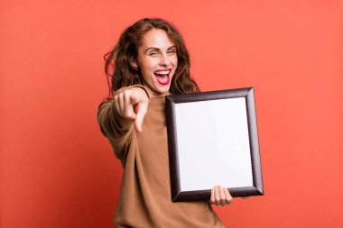 hispanic pretty woman pointing at camera choosing you with an empty blank frame