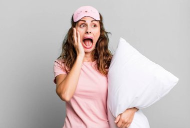hispanic pretty woman feeling happy, excited and surprised wearing pajamas and a pillow