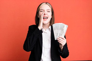 young pretty woman feeling happy,giving a big shout out with hands next to mouth. dollar banknotes