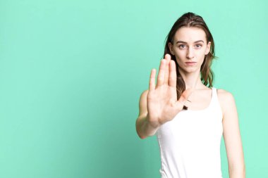 Genç ve güzel bir kadın ciddi görünüyor. Avuç içini gösteriyor. Dur hareketi yapıyor.