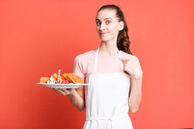 Genç ve güzel bir kadın kendini mutlu hissediyor ve heyecanlı bir şekilde kendini işaret ediyor. Waffle konsepti