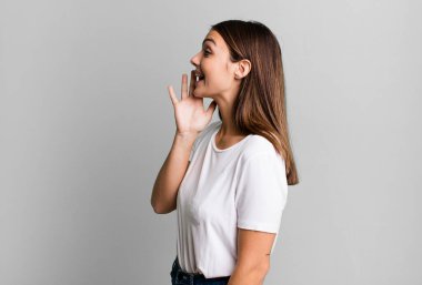 pretty young adult woman profile view, looking happy and excited, shouting and calling to copy space on the side